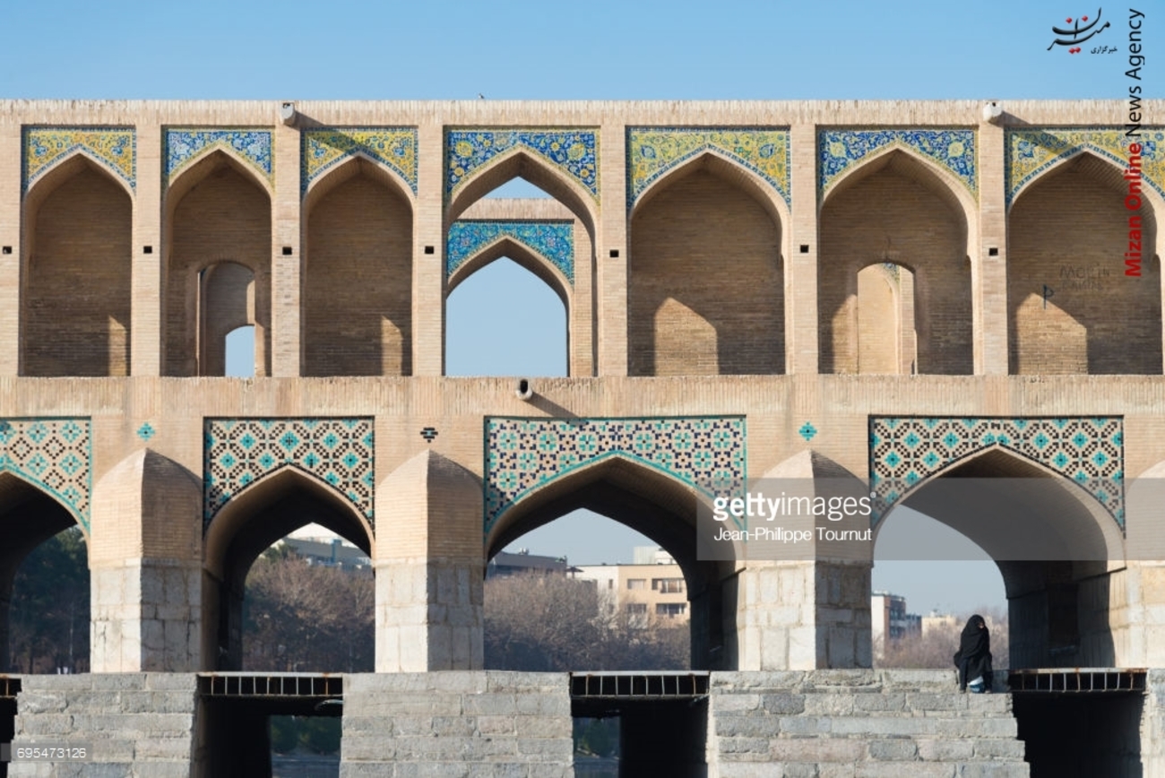 یک زن حجاب سنتی ایران یعنی چادر را بر سر کرده و در یکی از پله های پل خواجو نشسته است.